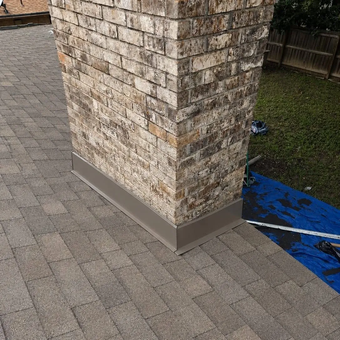 Brick chimney with metal flashing where it meets the shingles