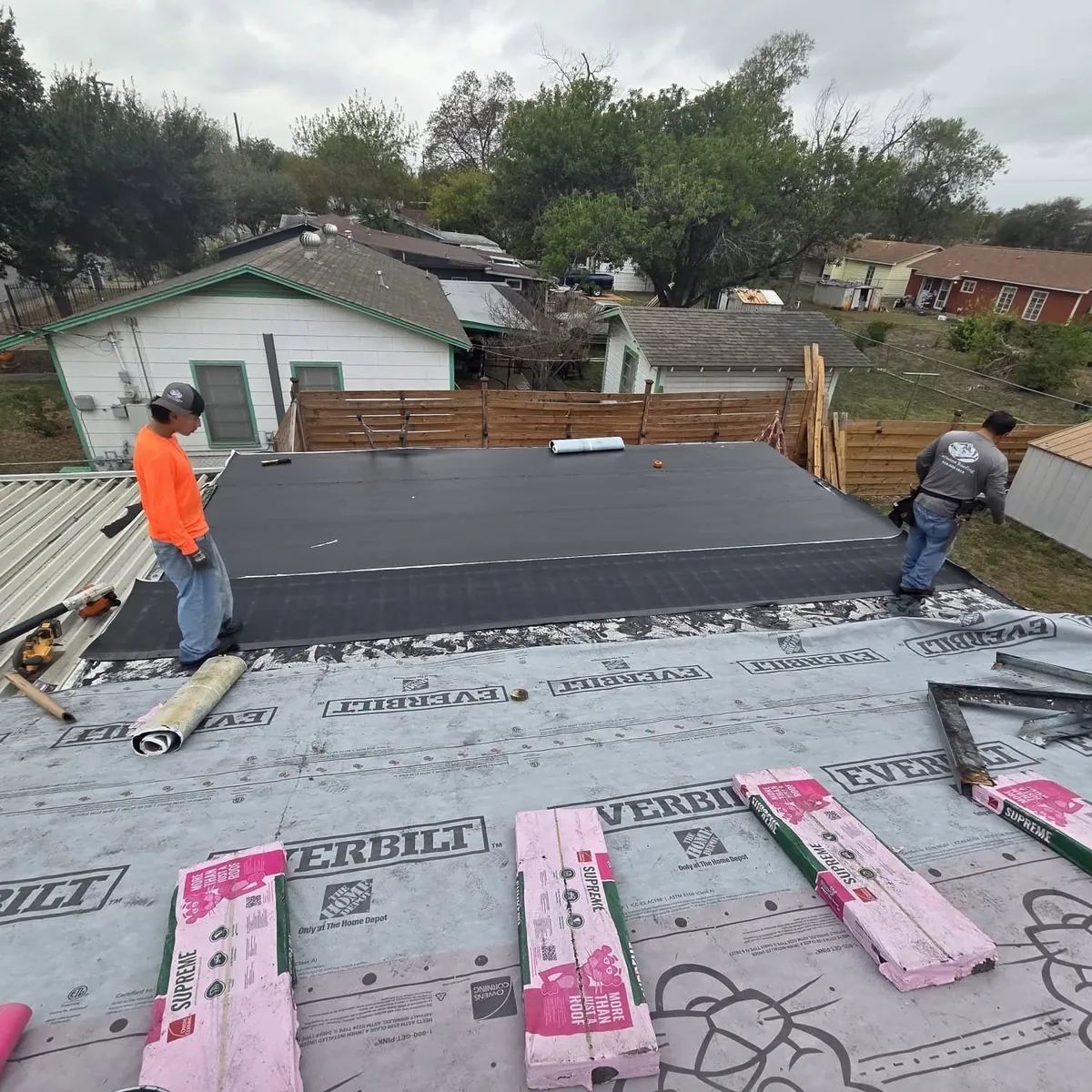 Two roofers rolling out underlayment on a stripped roof deck