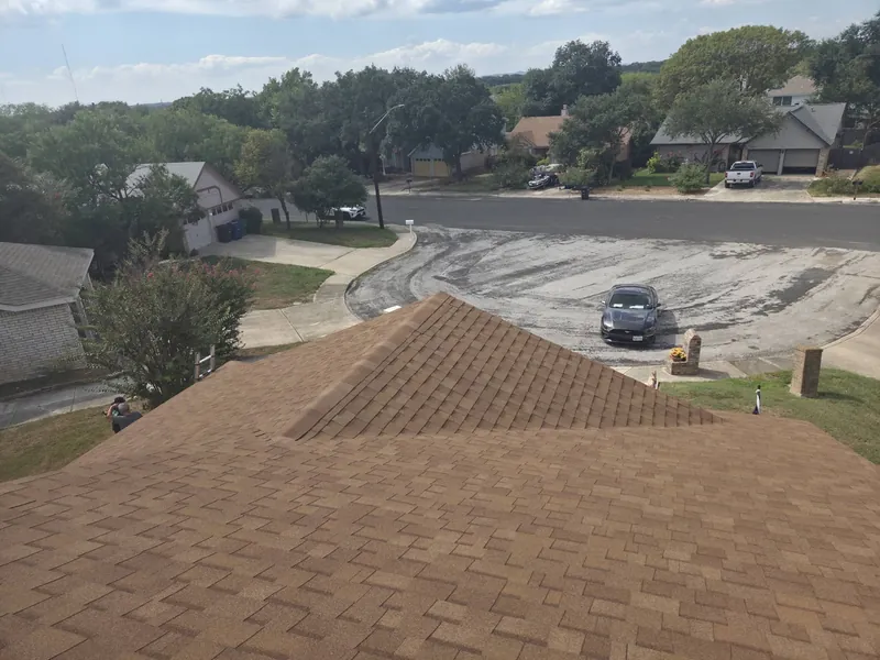 Newly installed tan shingle roof seen from the ridge, looking over a residential street