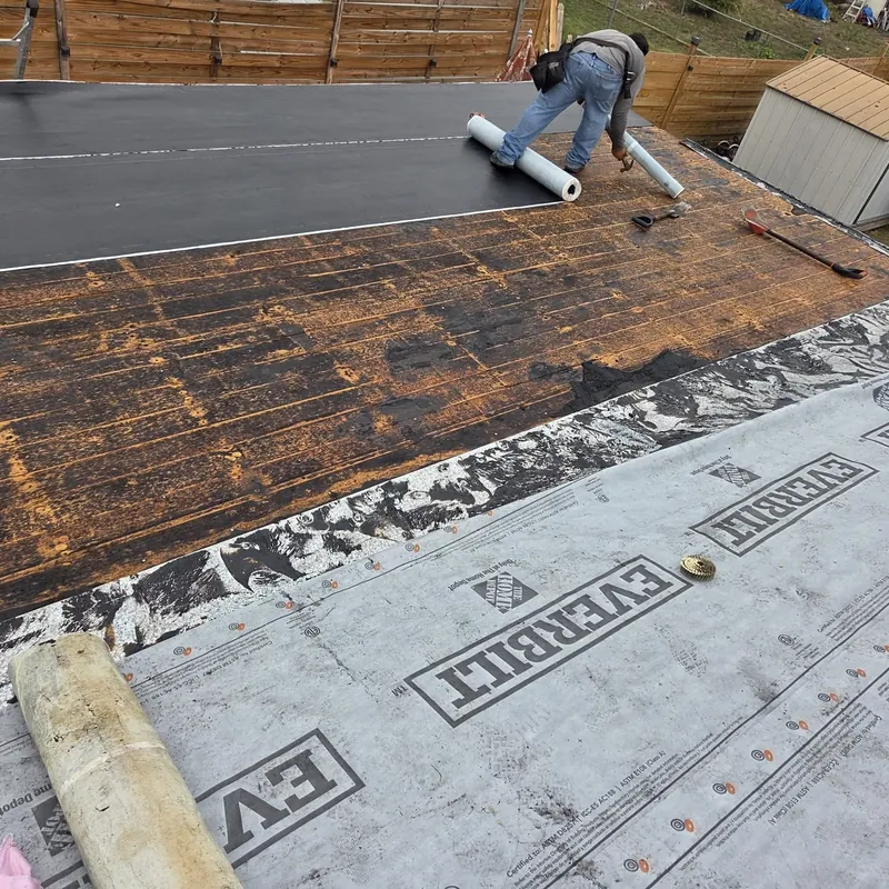 Roofer rolling out underlayment over the old roof deck after tear-off