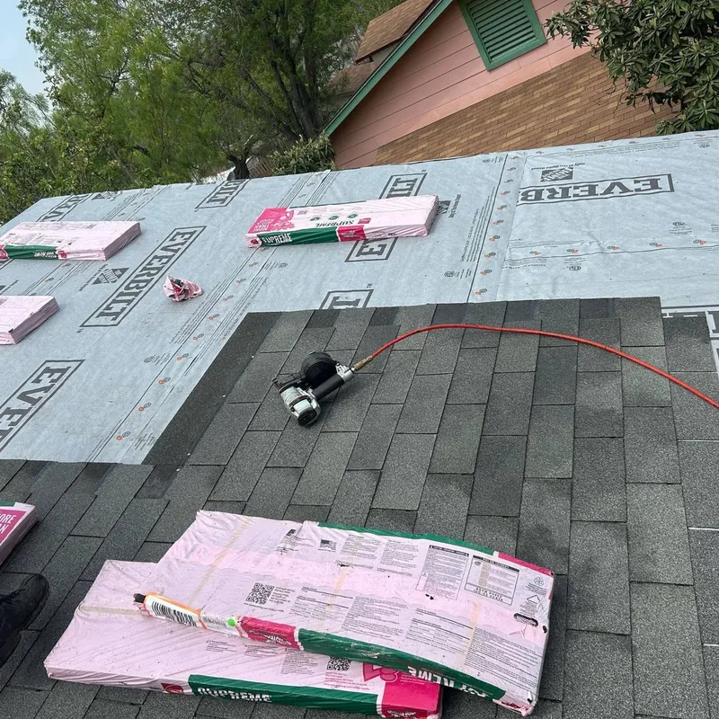 New charcoal shingles going on over synthetic underlayment, with a roofing nail gun and a shingle bundle