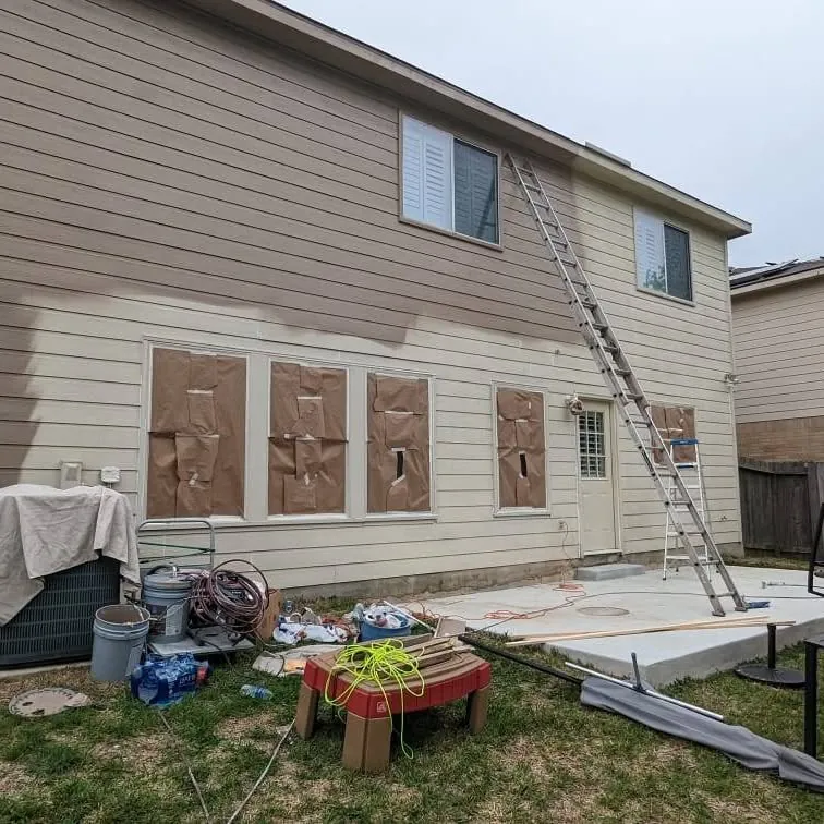 Two-story house with windows masked off for exterior painting, ladder against the wall