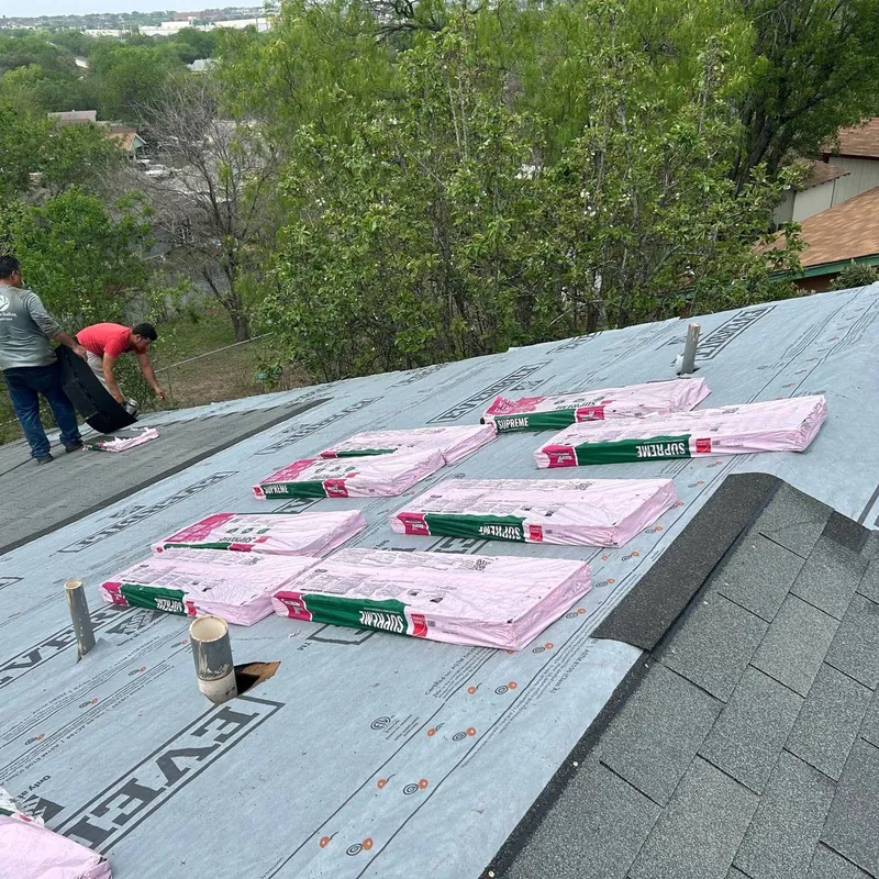 Synthetic underlayment with shingle bundles staged across the roof, two crew members at the edge